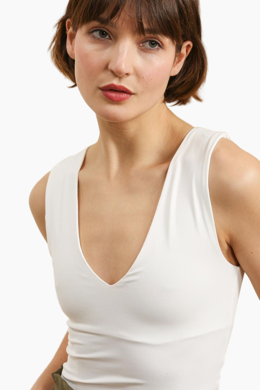 Woman wearing a white tank top against a plain background
