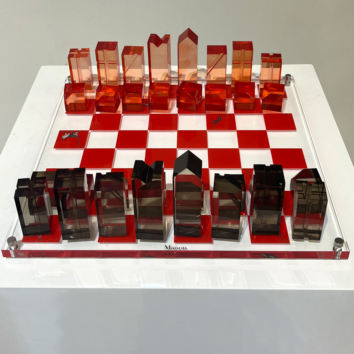 Transparent red and black chess set on a white chessboard with a gray background