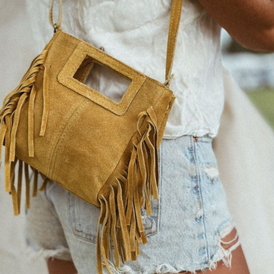 Brown suede handbag with fringe details worn by a person.