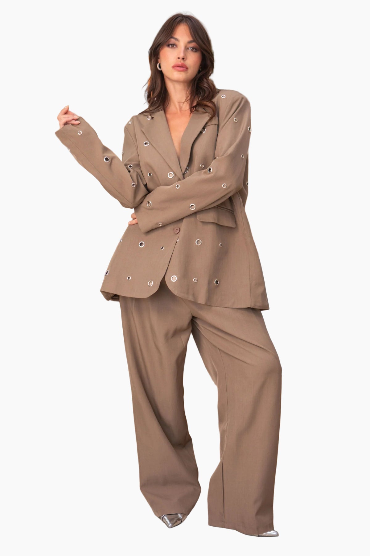 Woman in a beige suit standing in a room with a fireplace and plants.