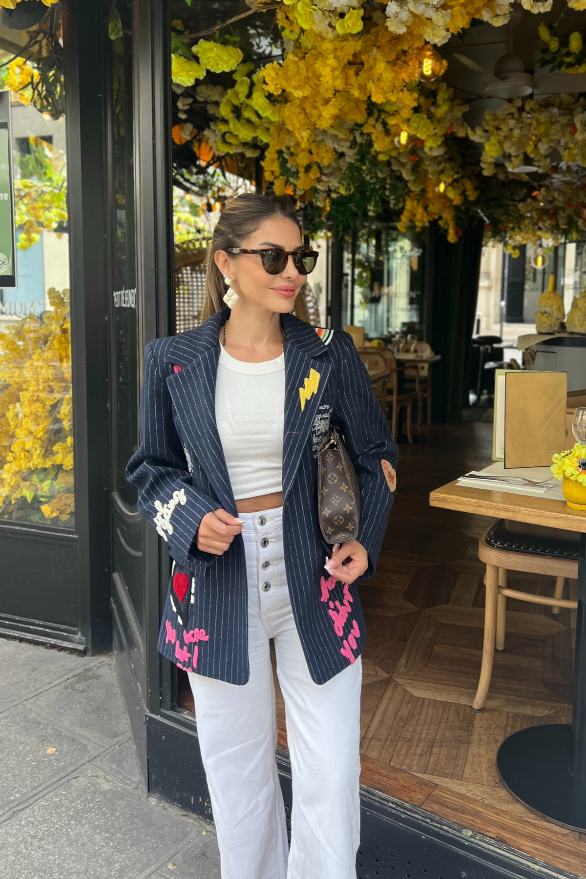 Woman in a stylish outfit standing outside a cafe with floral decorations.