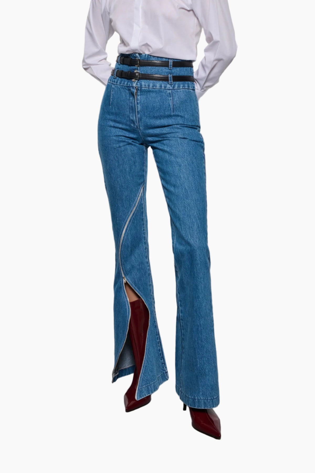 Person wearing blue flared jeans with a white shirt and red shoes on a plain background