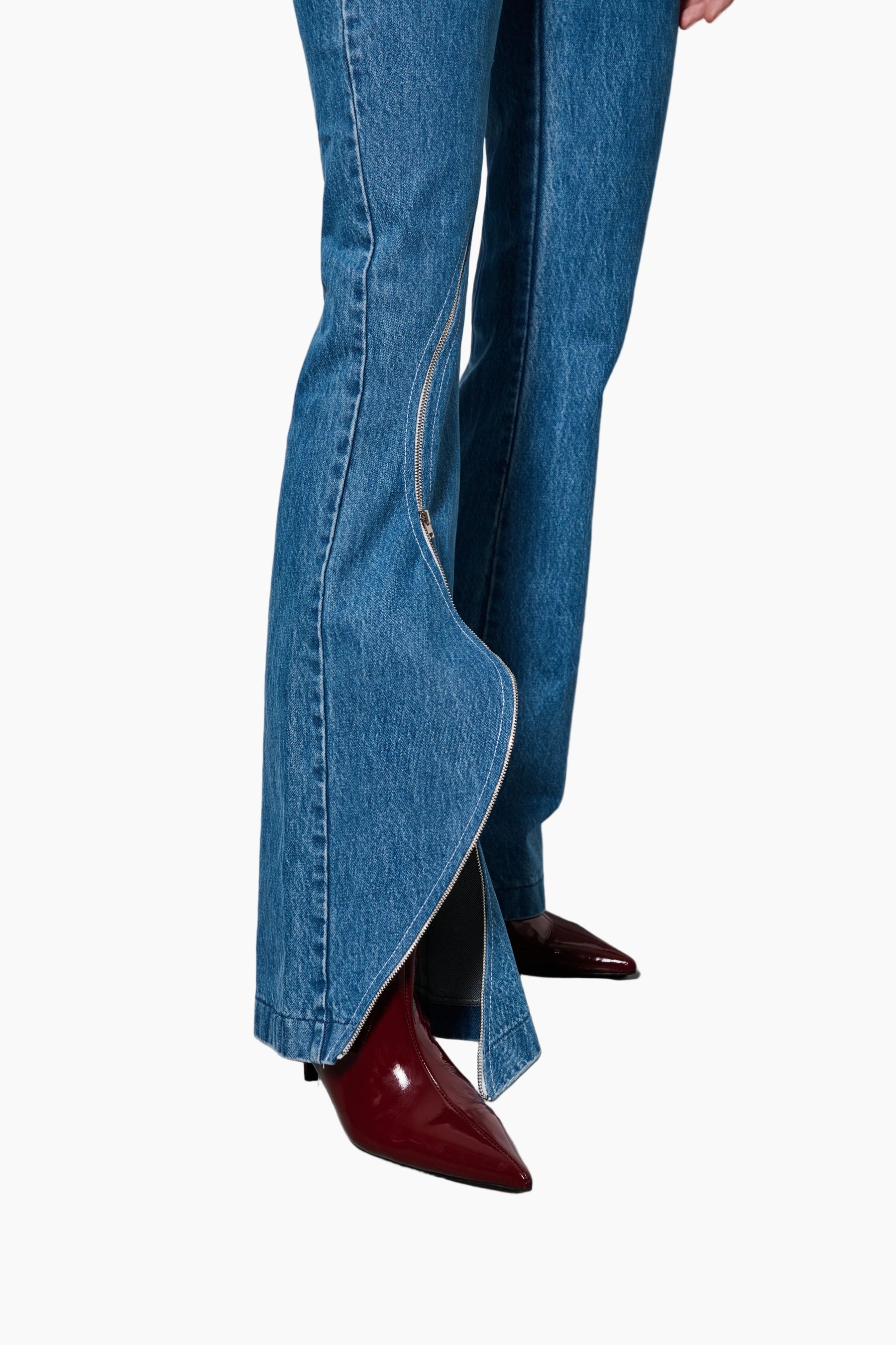 Blue jeans with a high slit and red shoes on a gray floor.