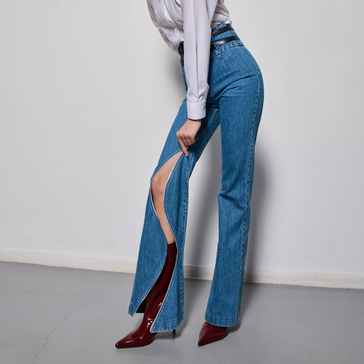 Person wearing blue flared jeans with a white shirt and red shoes on a plain background