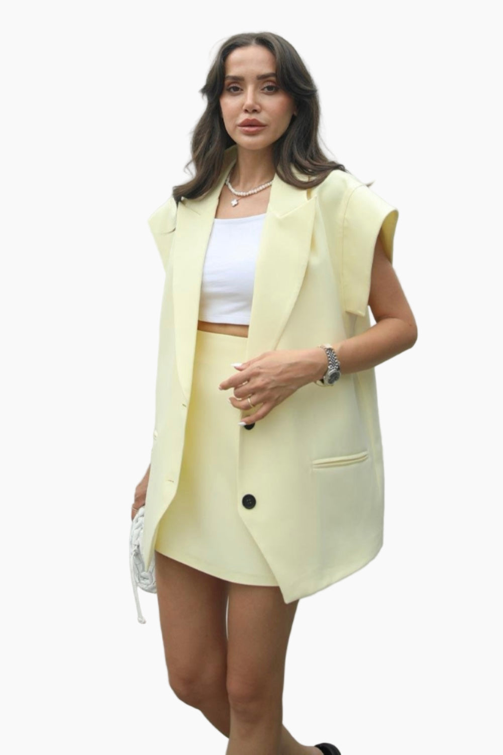 Woman wearing a light yellow blazer over a white top and skirt on a white background