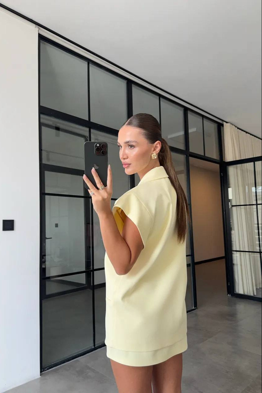Woman in a yellow dress taking a mirror selfie in an office setting