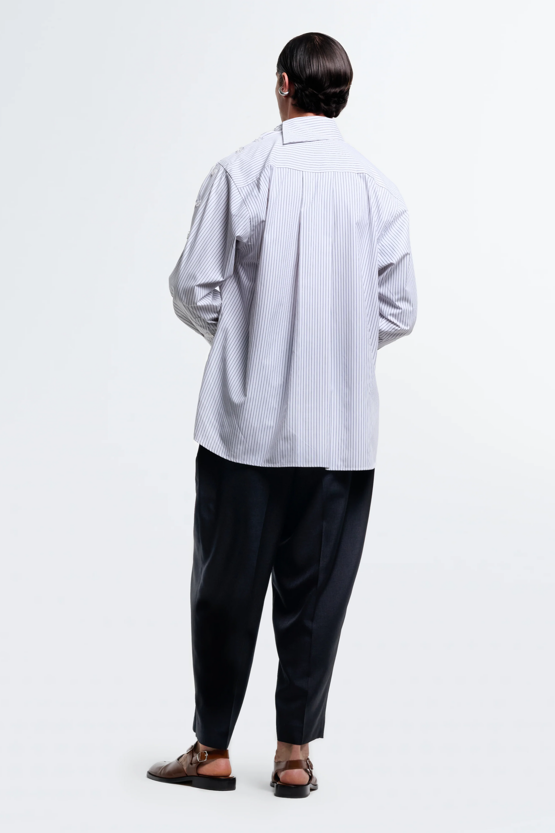 Person wearing a light gray striped shirt and dark pants on a white background