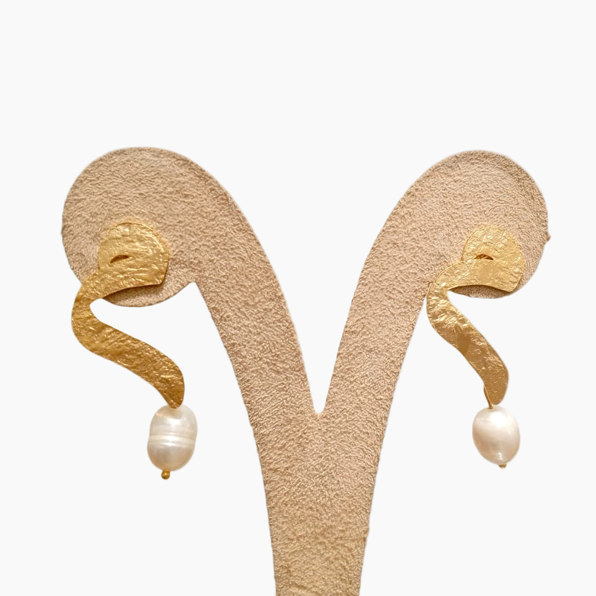 Gold earrings with pearl drops on a beige stand against a white background