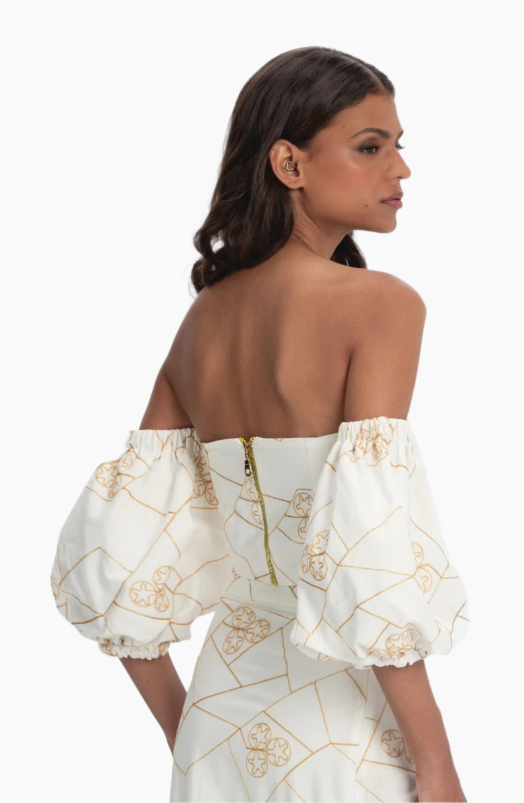 Woman wearing a white dress with gold patterns and puffed sleeves