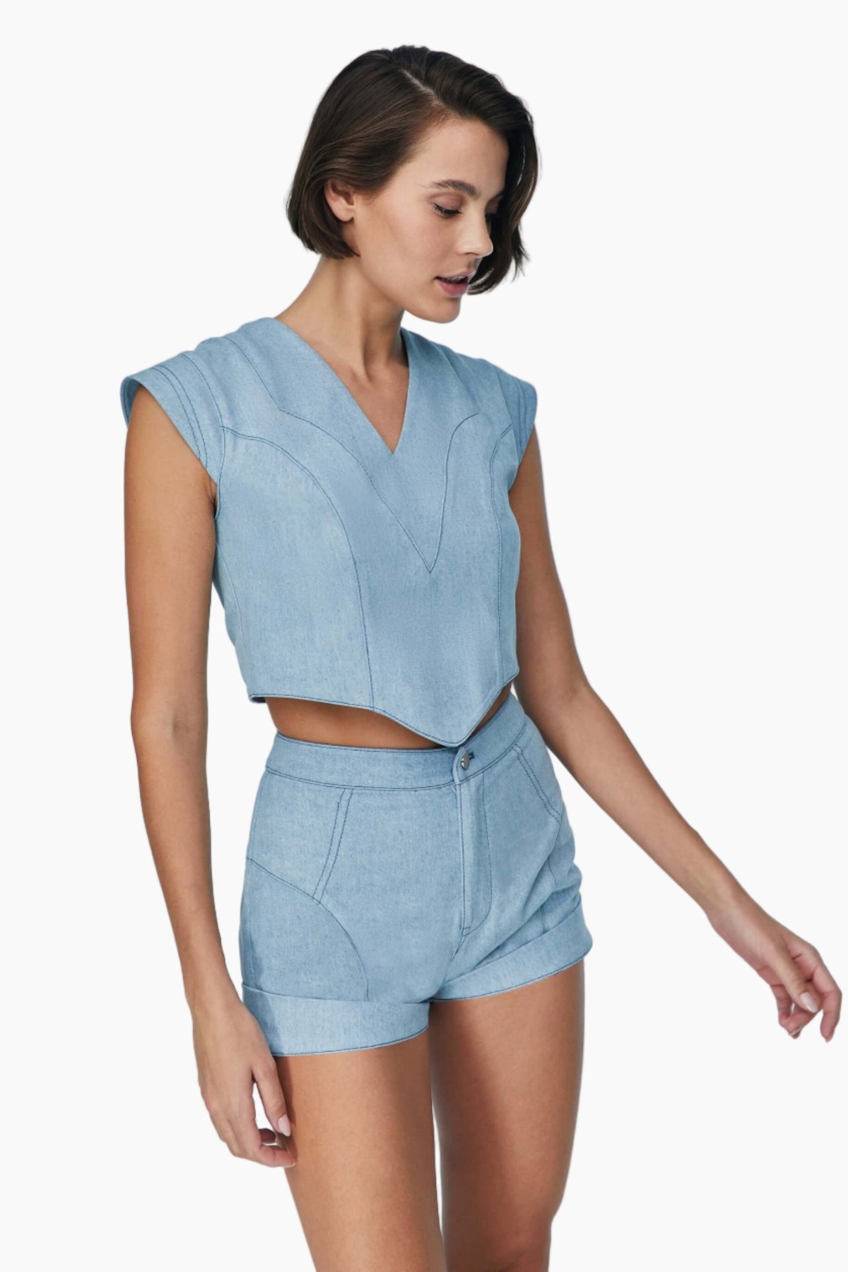 Woman wearing a light blue sleeveless top and shorts set. denim short Feature mid rise belt. It is secured with a metallic button and a zipper fastening.