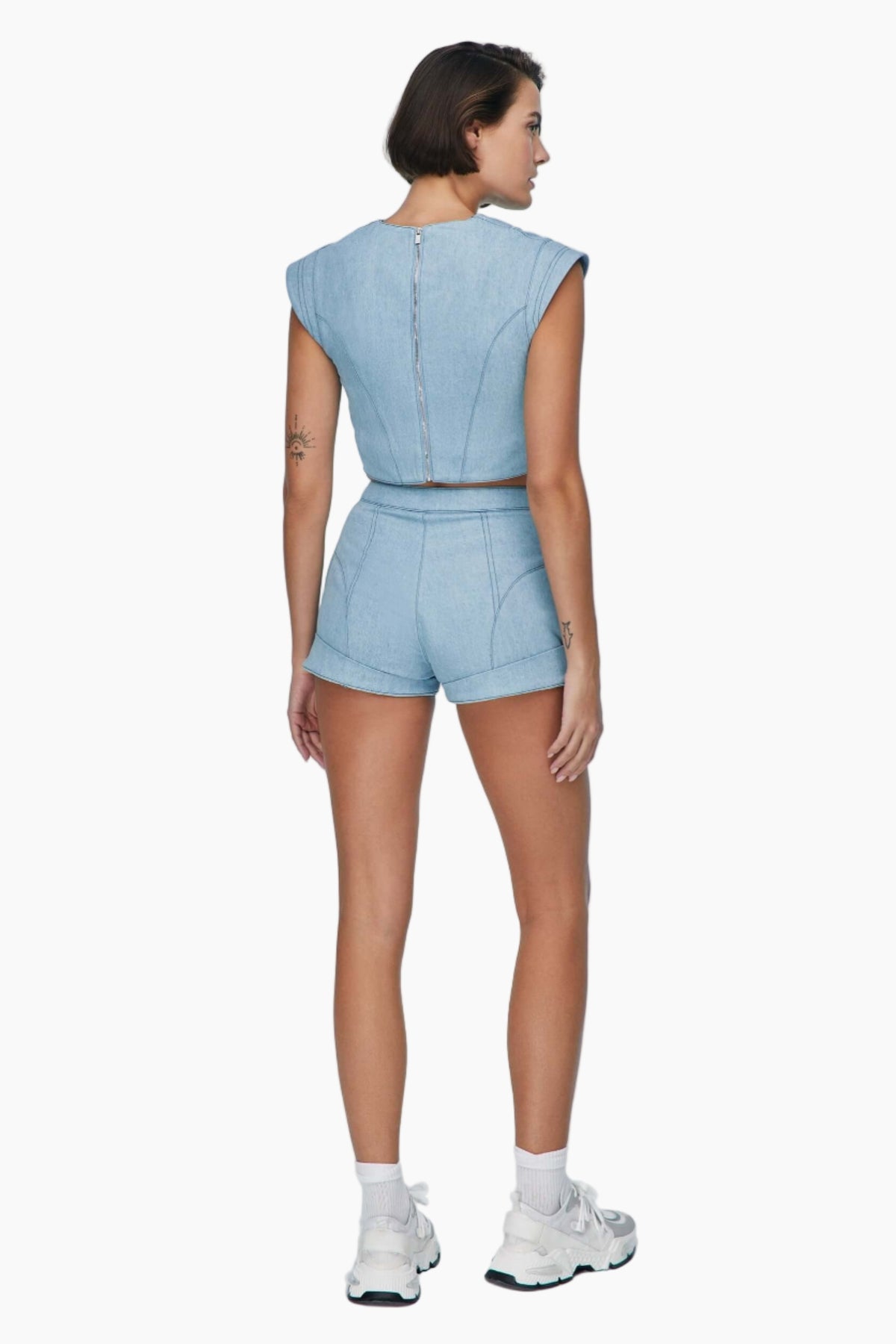 Woman wearing a light blue denim outfit. denim short Feature mid-rise belt. It is secured with a metallic button and a zipper fastening.