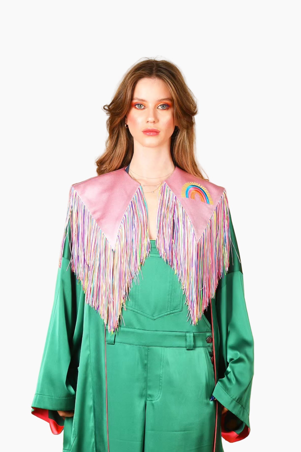 Woman wearing a pink jacket with colorful fringe and rainbow design on a white background