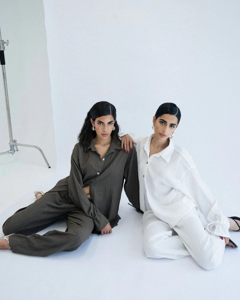 Two women sitting on a white floor, one in a green outfit and the other in a white outfit,