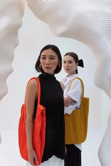 Two women holding colorful bags against a white, abstract background