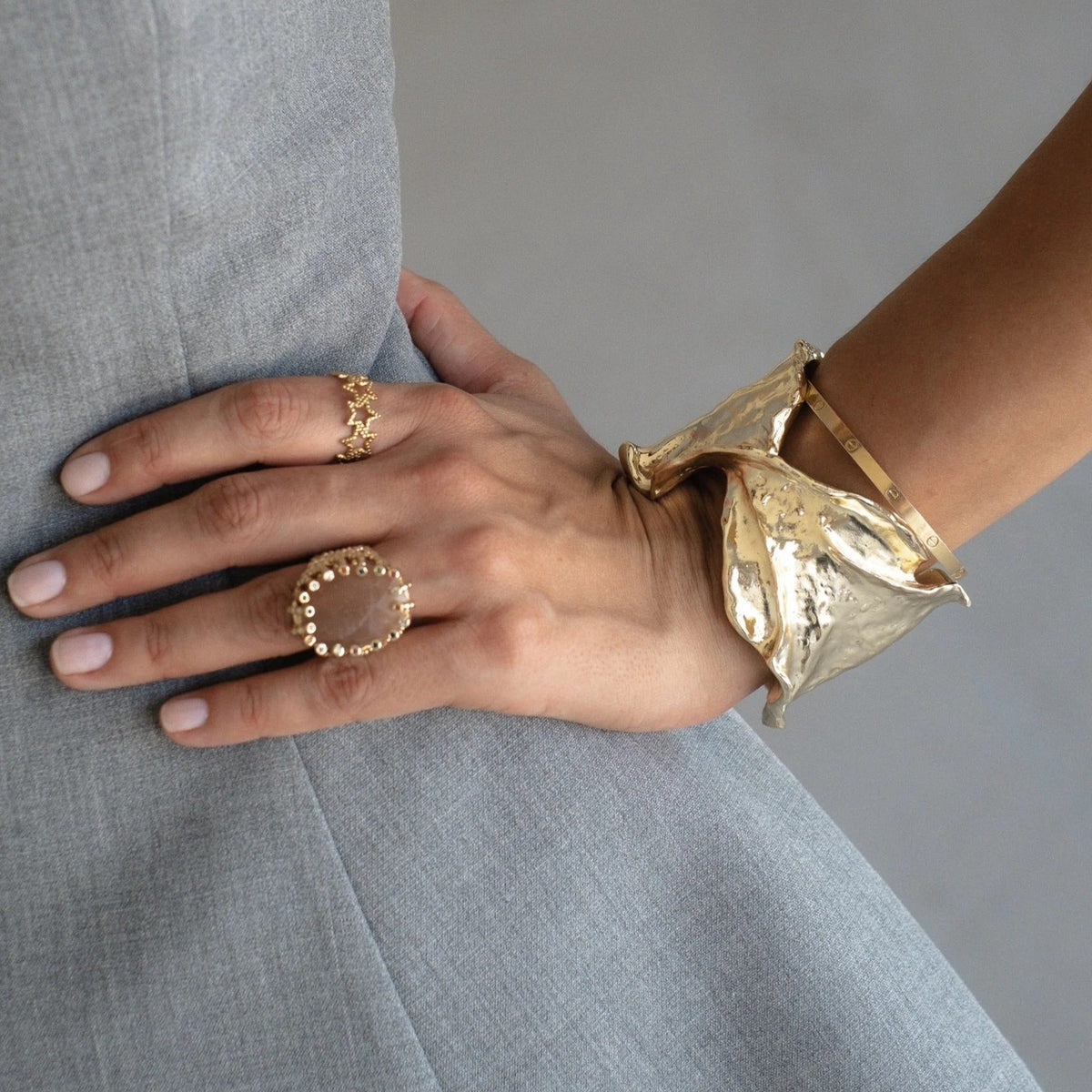 Hand wearing gold rings and a gold bracelet on a gray background