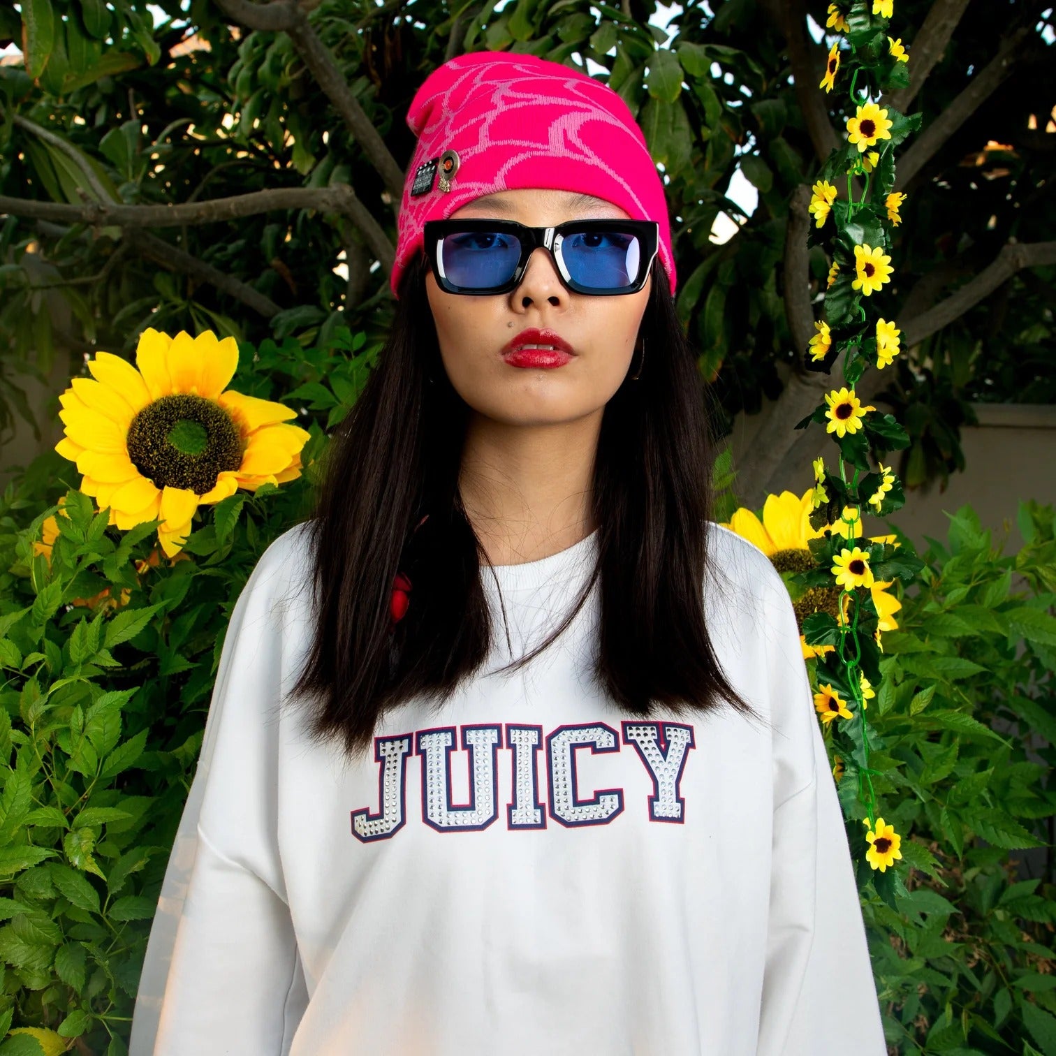 Person wearing a pink beanie and sunglasses with sunflowers in the background