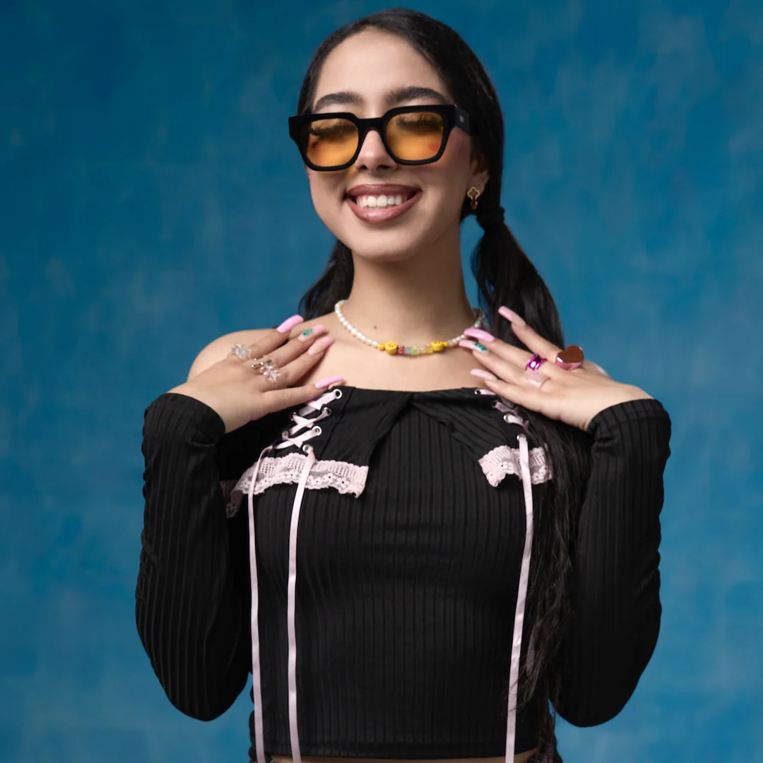 Woman wearing sunglasses and a black outfit with decorative elements against a blue background