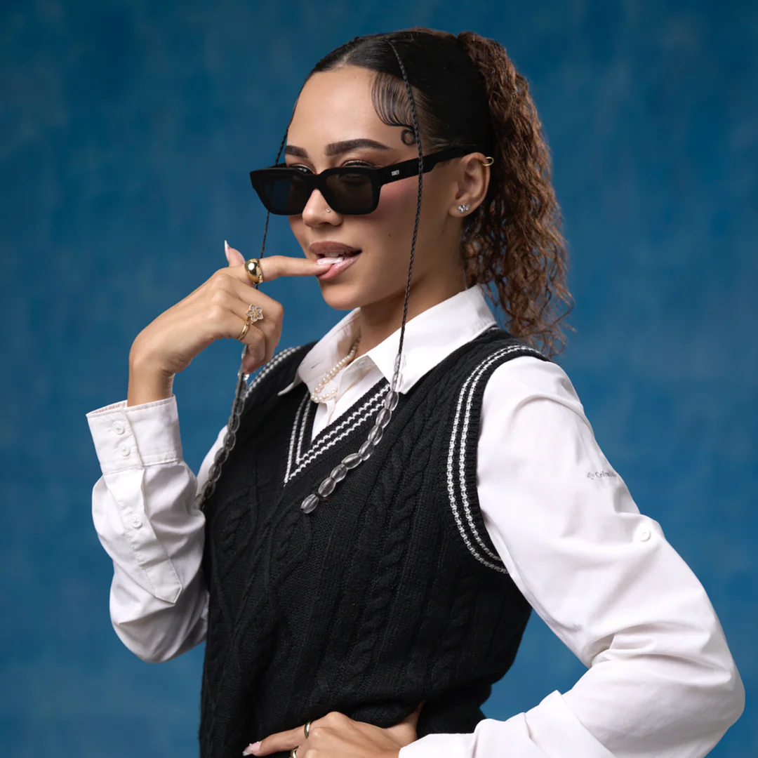 Woman wearing a black sweater vest over a white shirt with a blue background