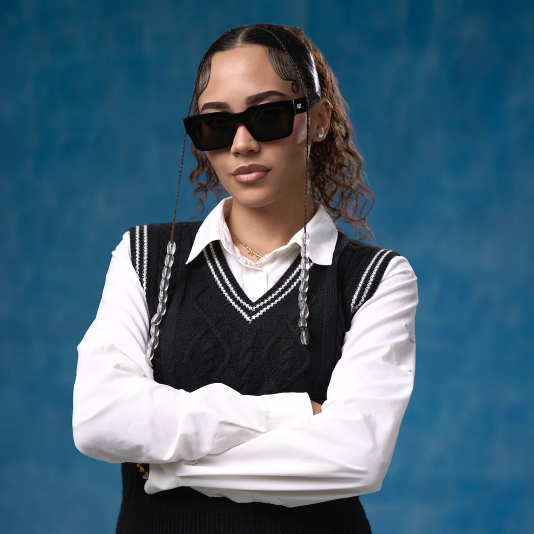 Person wearing a black sweater vest over a white shirt with arms crossed against a blue background