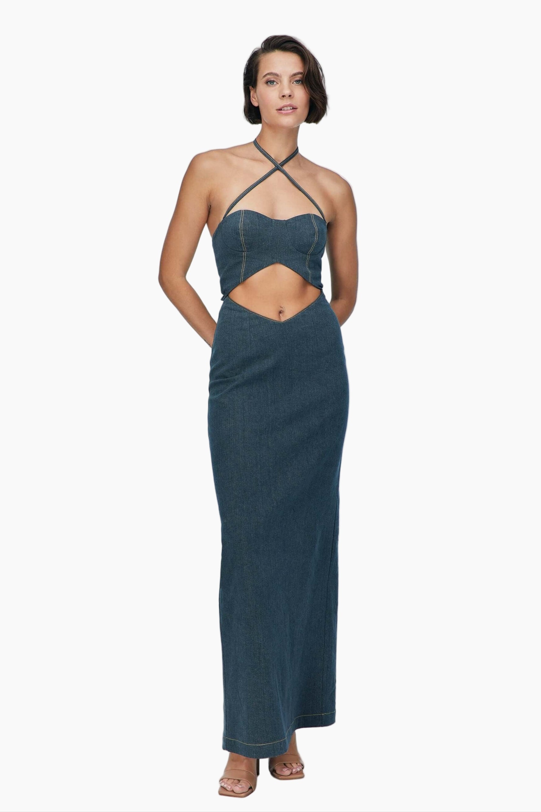 Woman wearing a blue denim maxi dress with delicate cross strap neck, metallic zipper closure and slit detail that extends to the back.