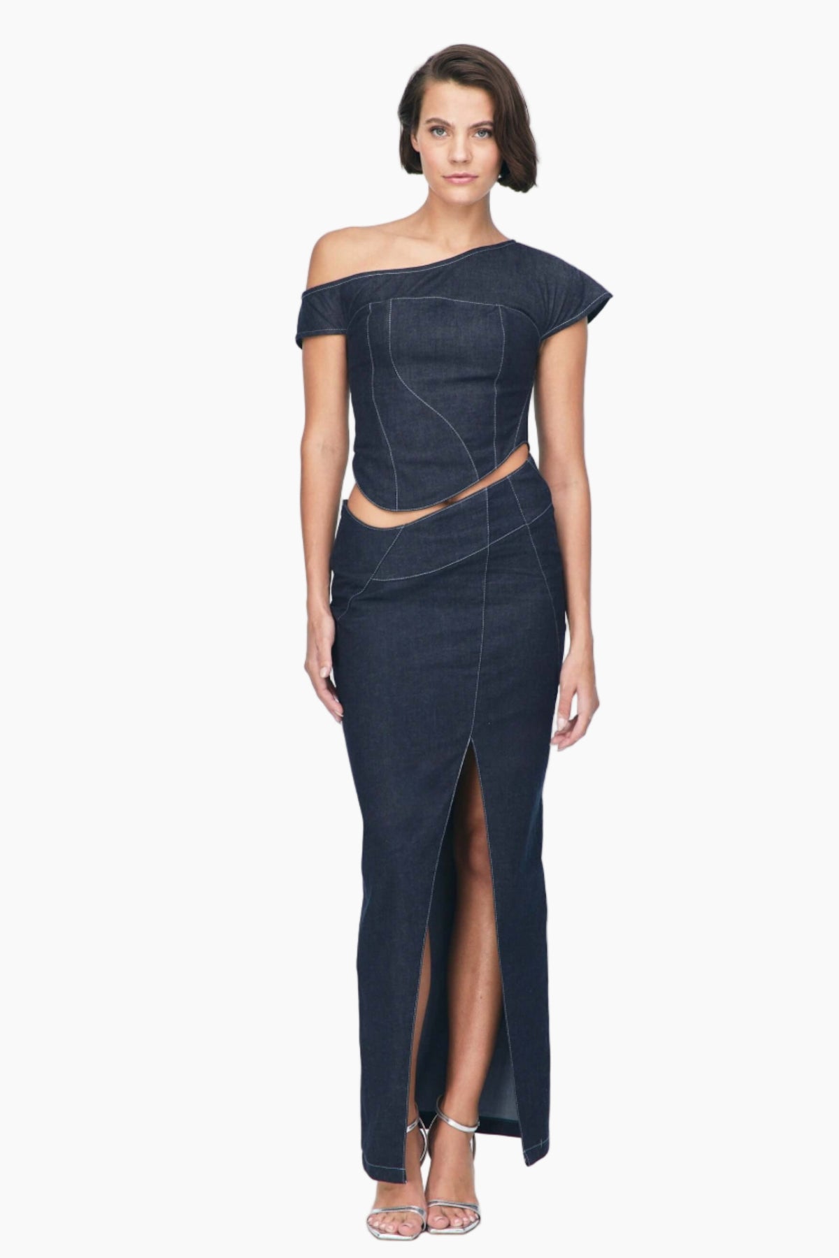 Woman wearing a dark blue off-shoulder top with a Vonk denim skirt features a mid-rise asymmetrical waist. One side slit .