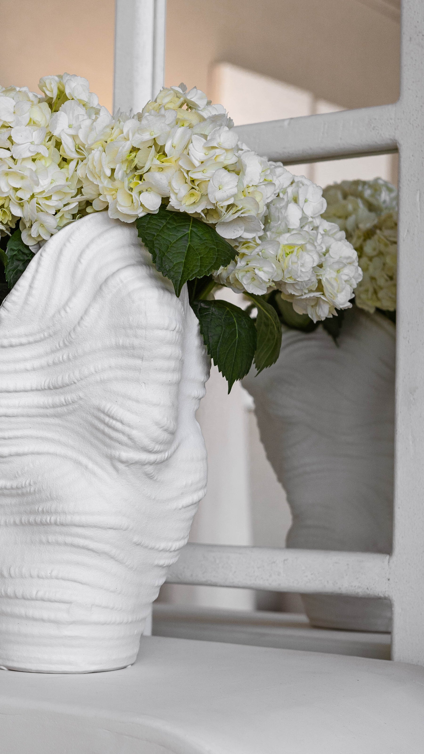 White textured vase with white flowers against a neutral background