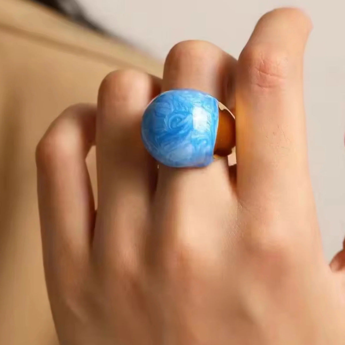 Hand wearing a blue ring with a marbled pattern on a neutral background
