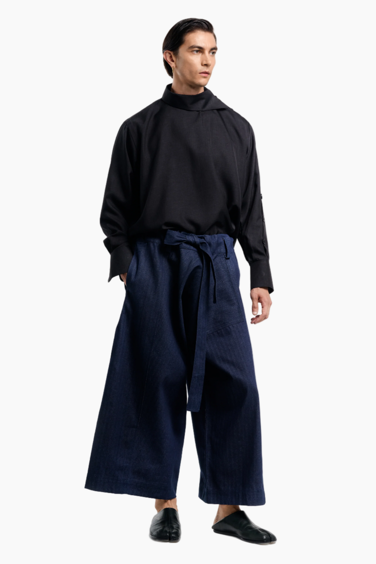 Man wearing a black turtleneck and navy wide-leg pants on a white background