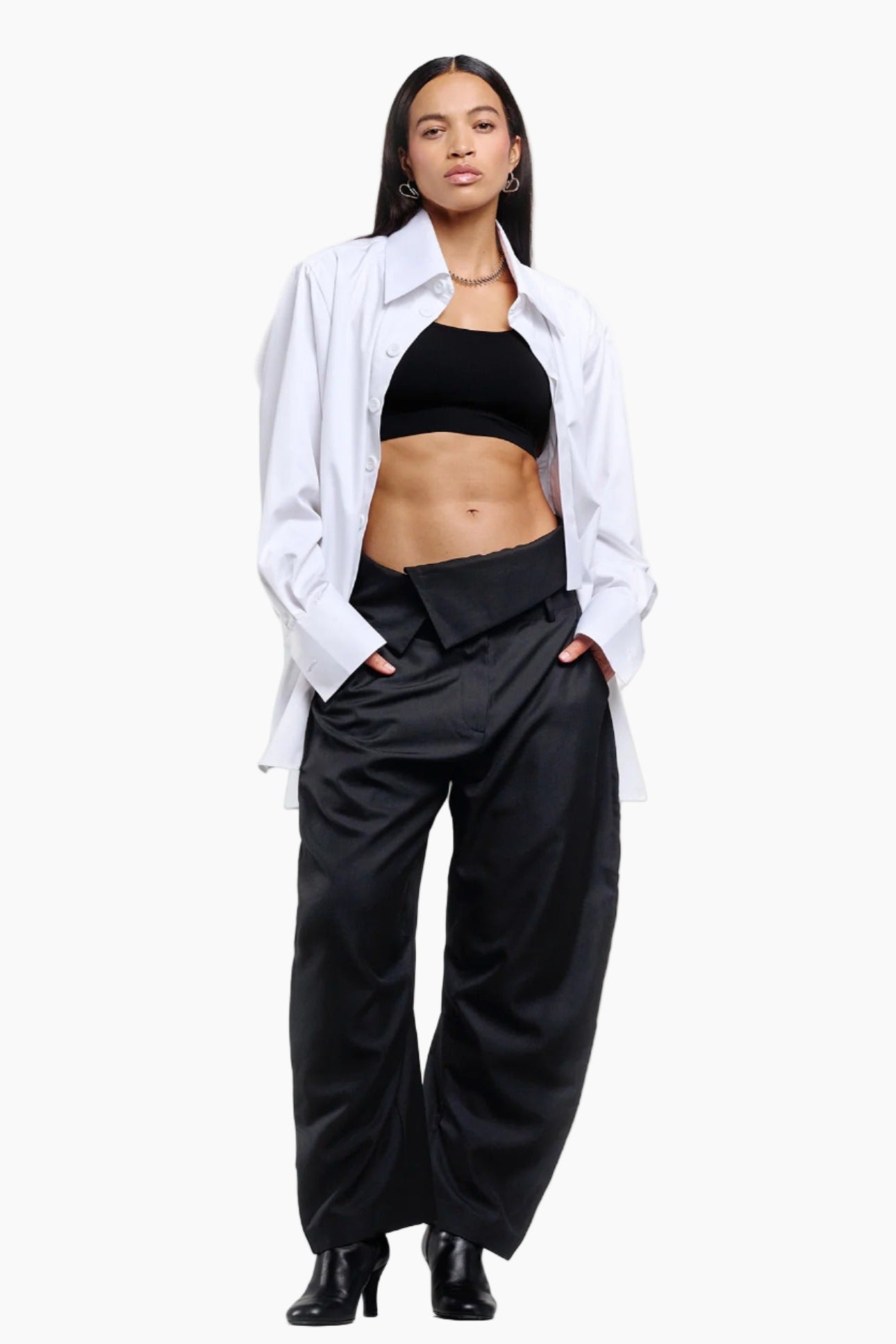 Woman wearing a white shirt over a black top and wide-leg black pants on a white background