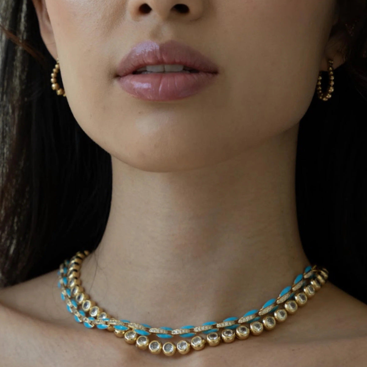 Close-up of a woman wearing a gold necklace with blue accents and matching earrings.