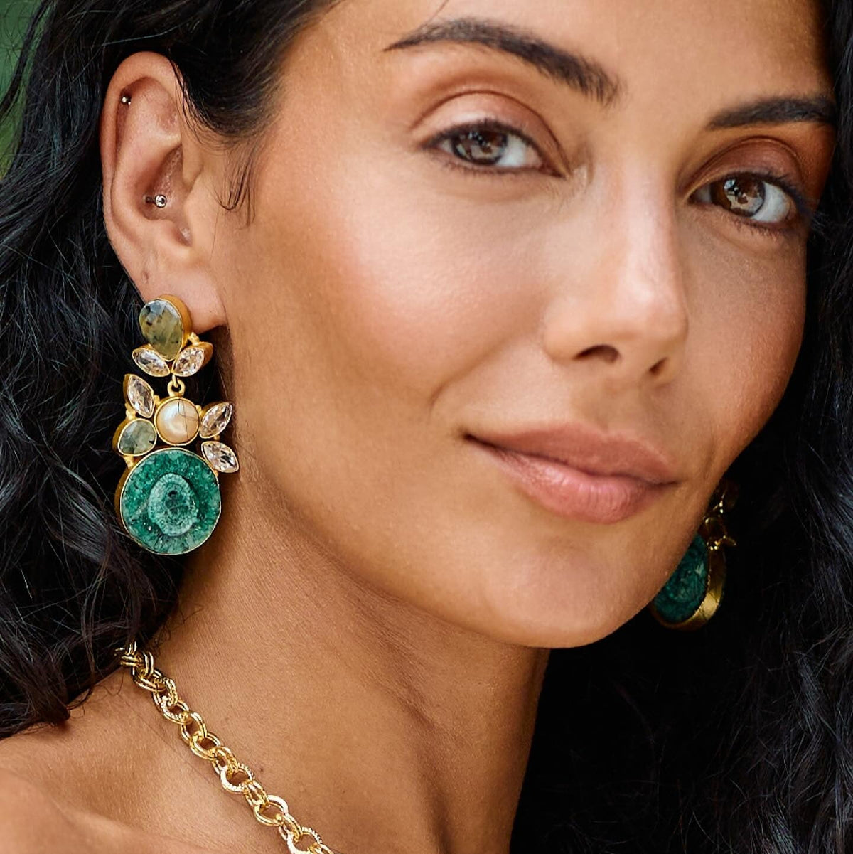 Close-up of a woman wearing gold and green earrings with a blurred background