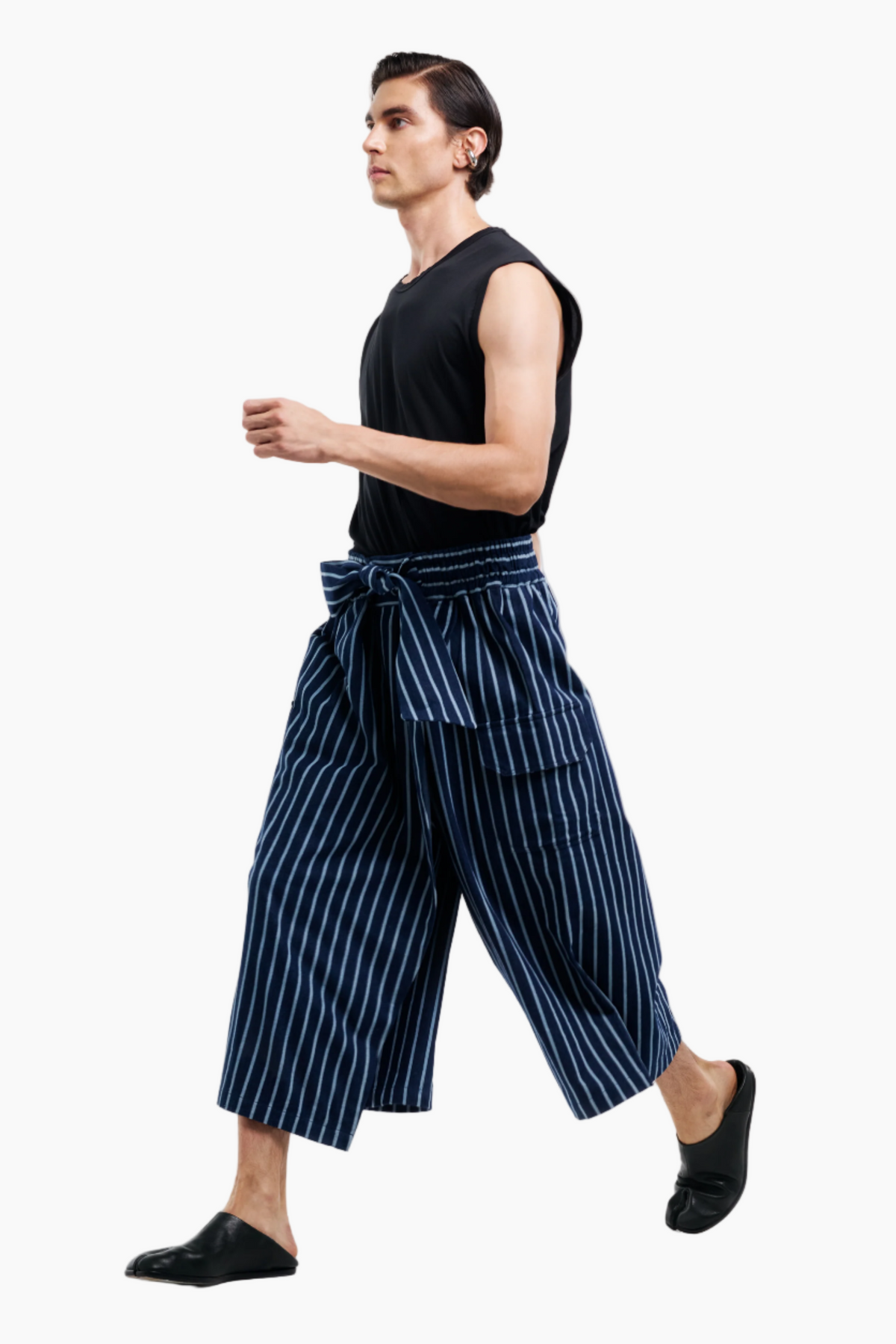 Person wearing a black sleeveless top and blue striped pants on a white background