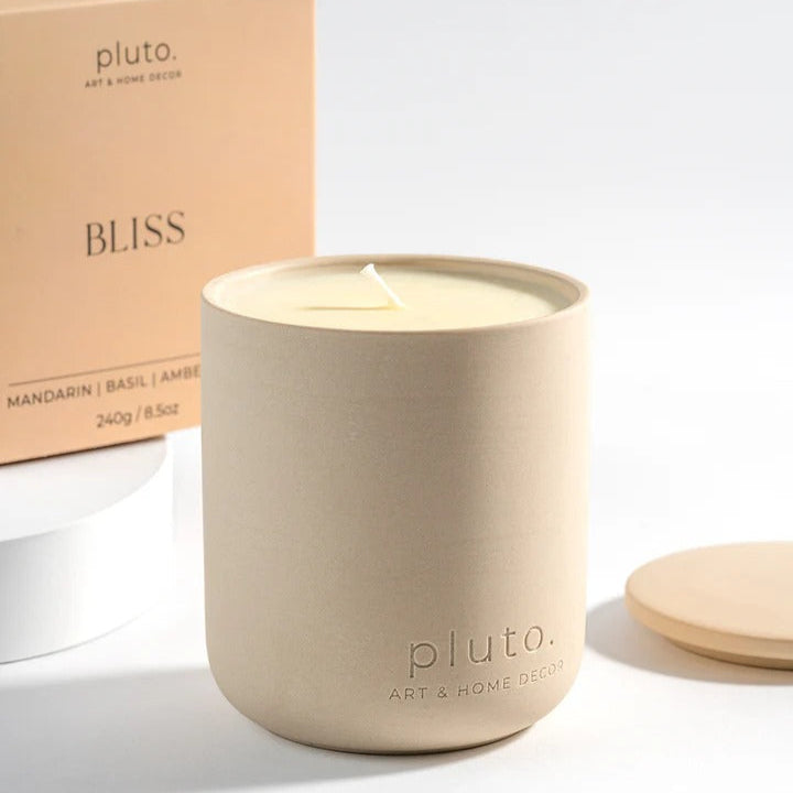 Beige candle with 'pluto.' branding and a box labeled 'BLISS' in the background.