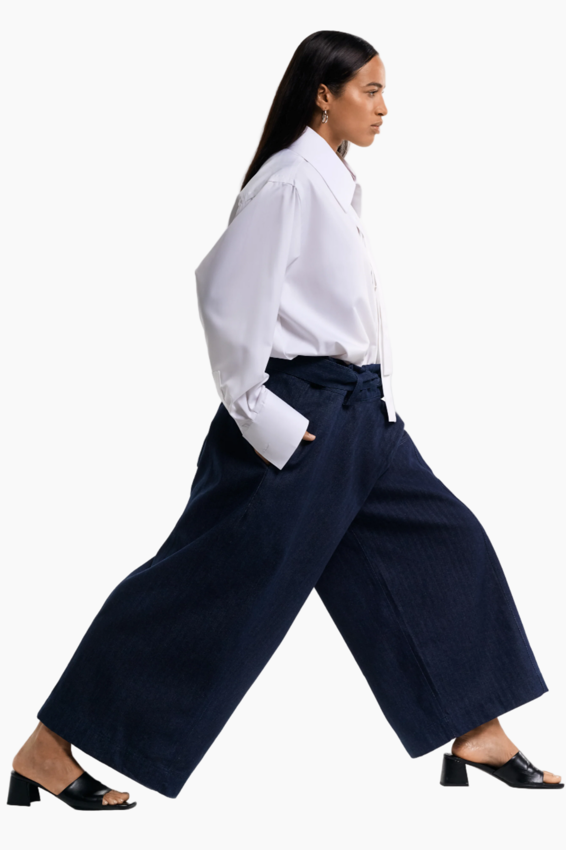 Woman wearing a white shirt and navy wide-leg pants on a white background
