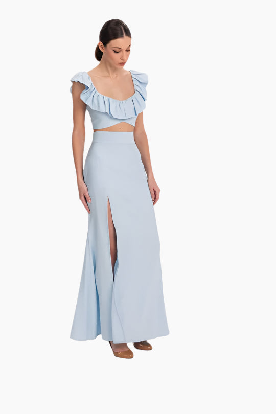 linen set featuring a charming top and skirt ensemble. The top boasts delicate ruffles adorning the neckline. The skirt features a flattering high waist design with a slit in the front.