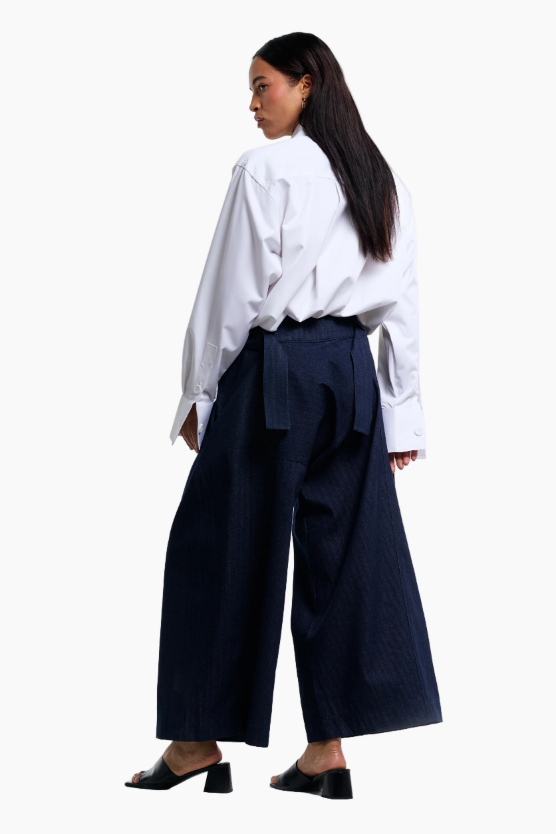 Woman wearing a white blouse and navy wide-leg pants on a white background