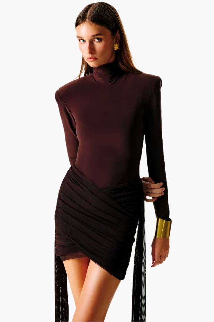 Woman wearing a dark brown long-sleeve top and black skirt with gold arm band