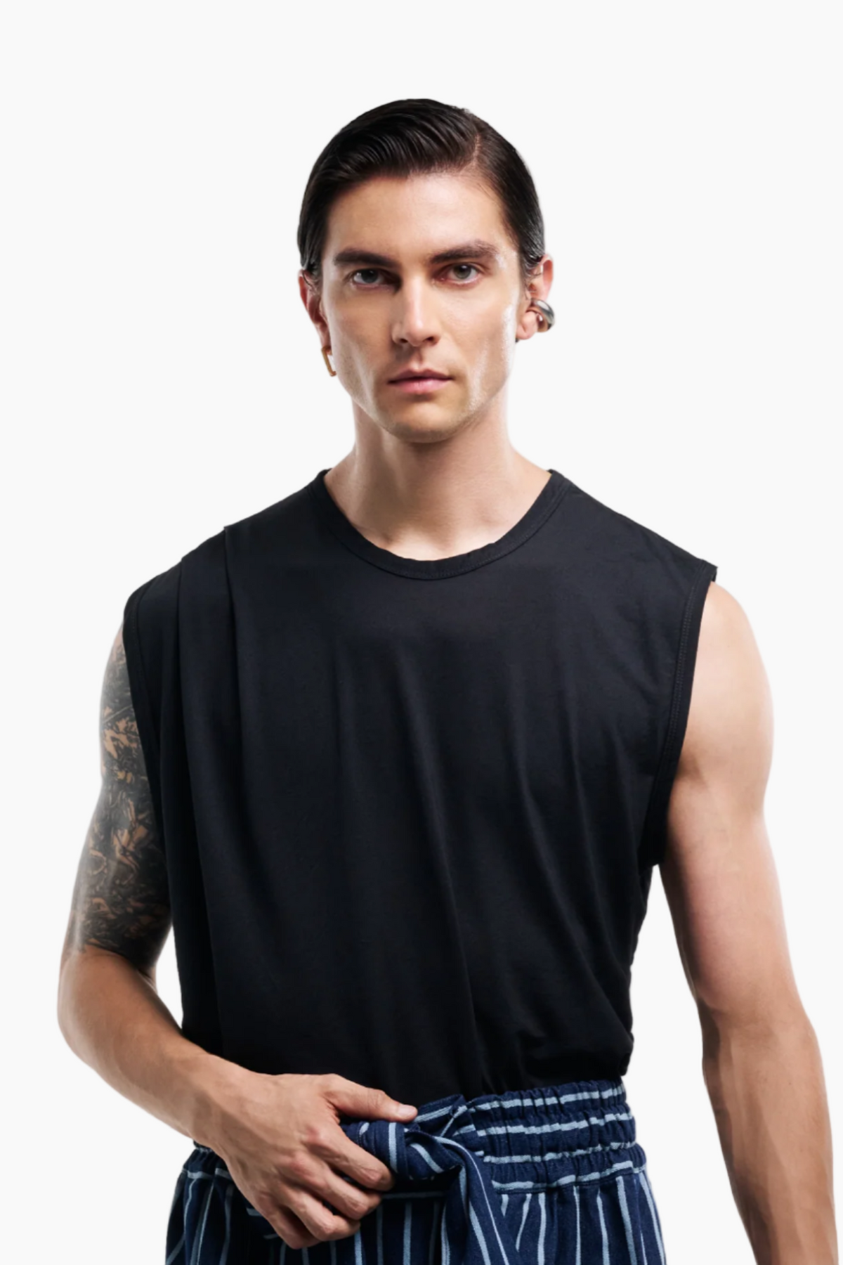 Man wearing a black sleeveless shirt and striped pants on a white background