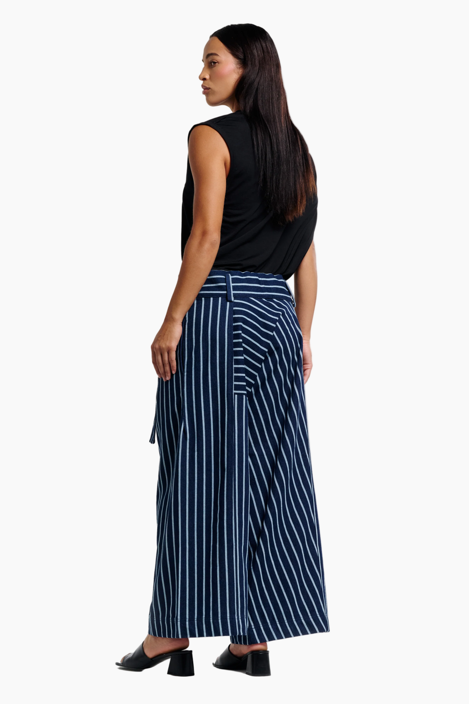 Woman wearing a black sleeveless top and blue striped pants on a white background