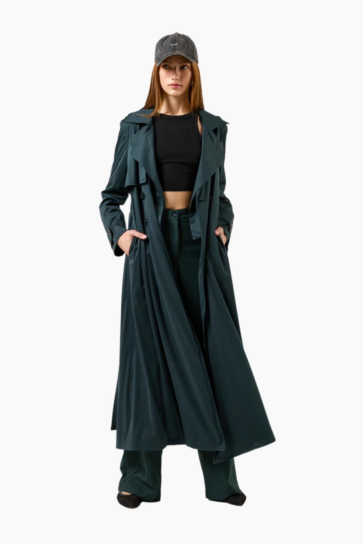 Woman wearing a long dark green coat and cap on a white background