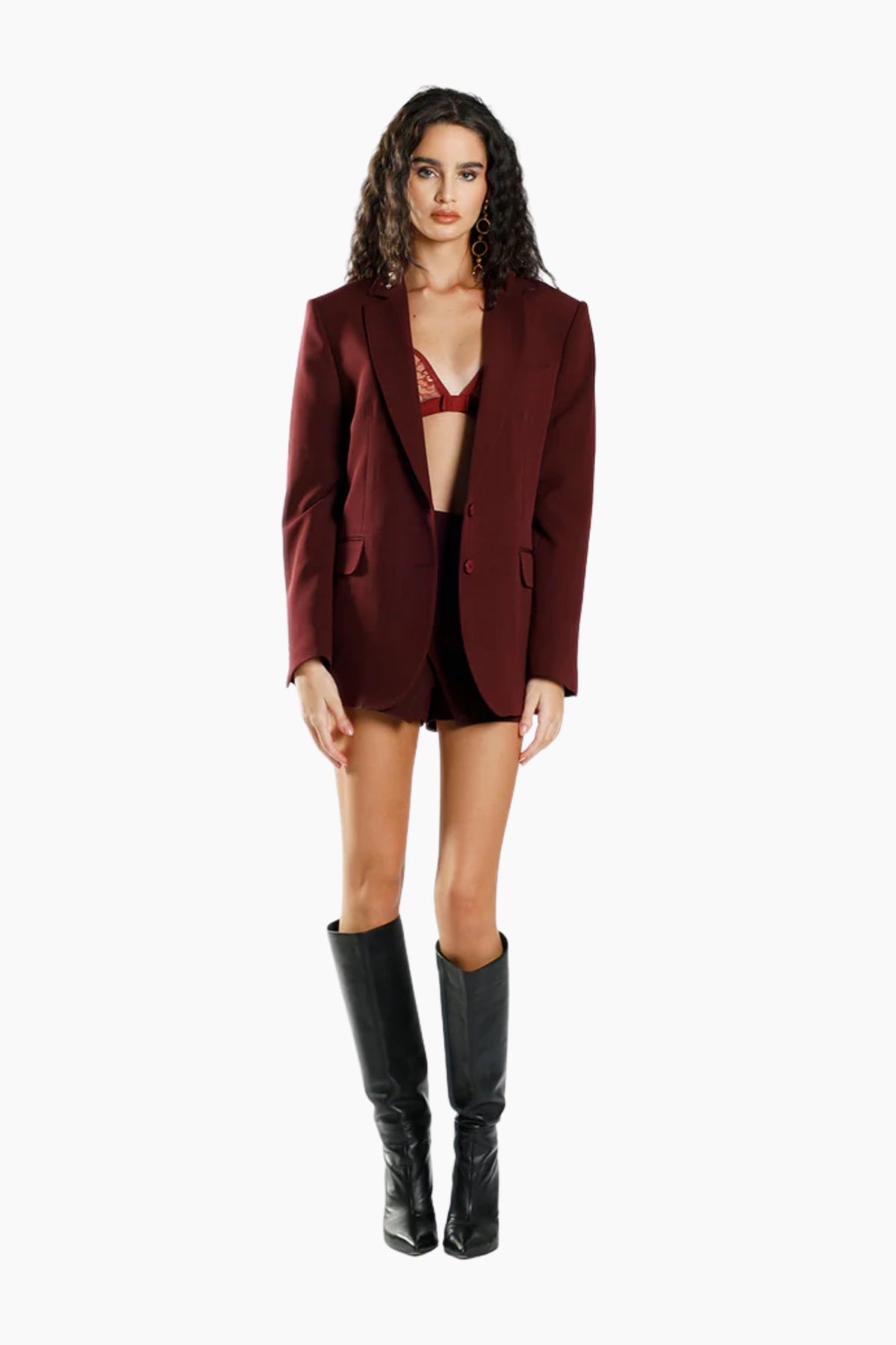 Woman wearing a burgundy blazer, black underwear, and black boots on a white background