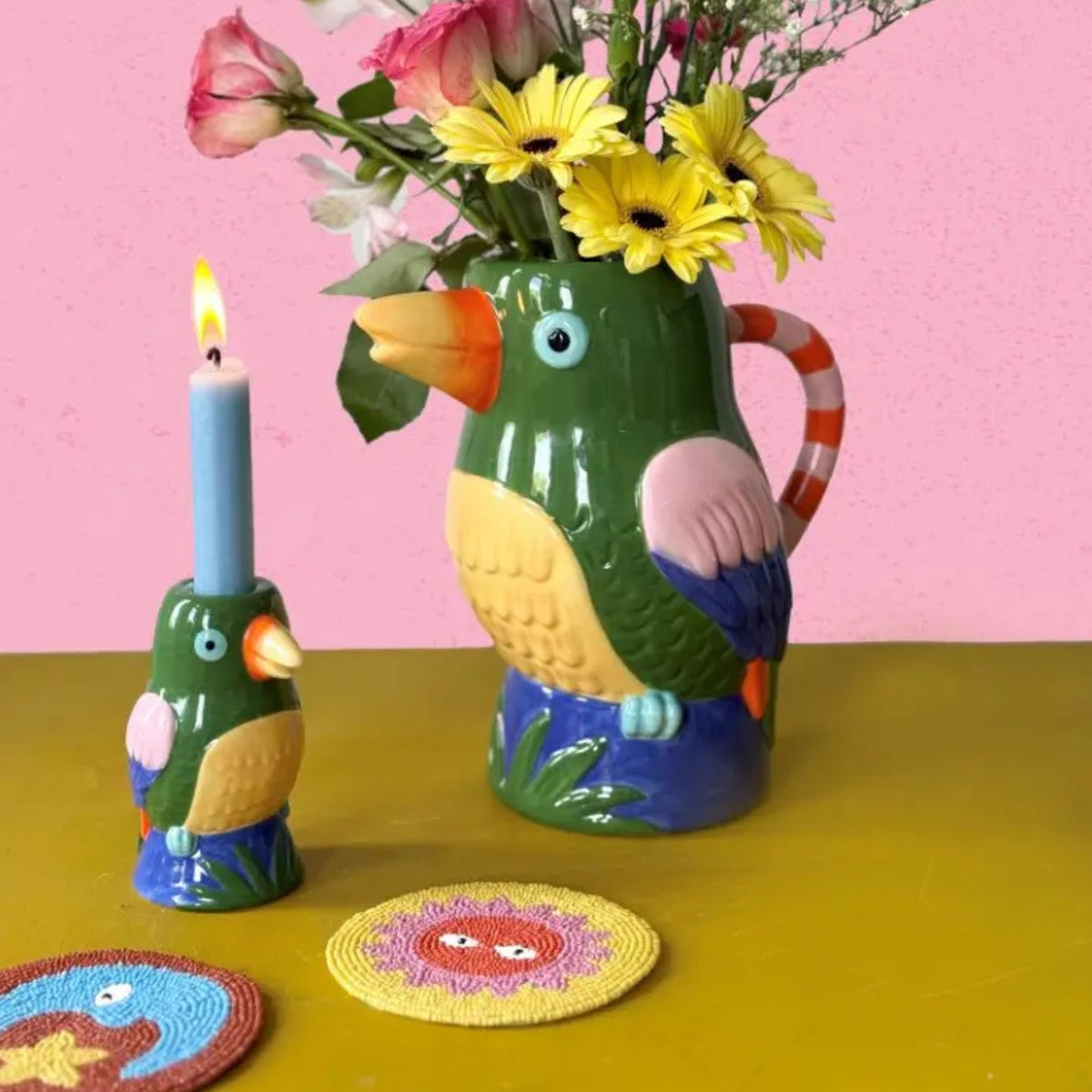 Colorful bird-shaped pitcher with flowers, candle, and coaster