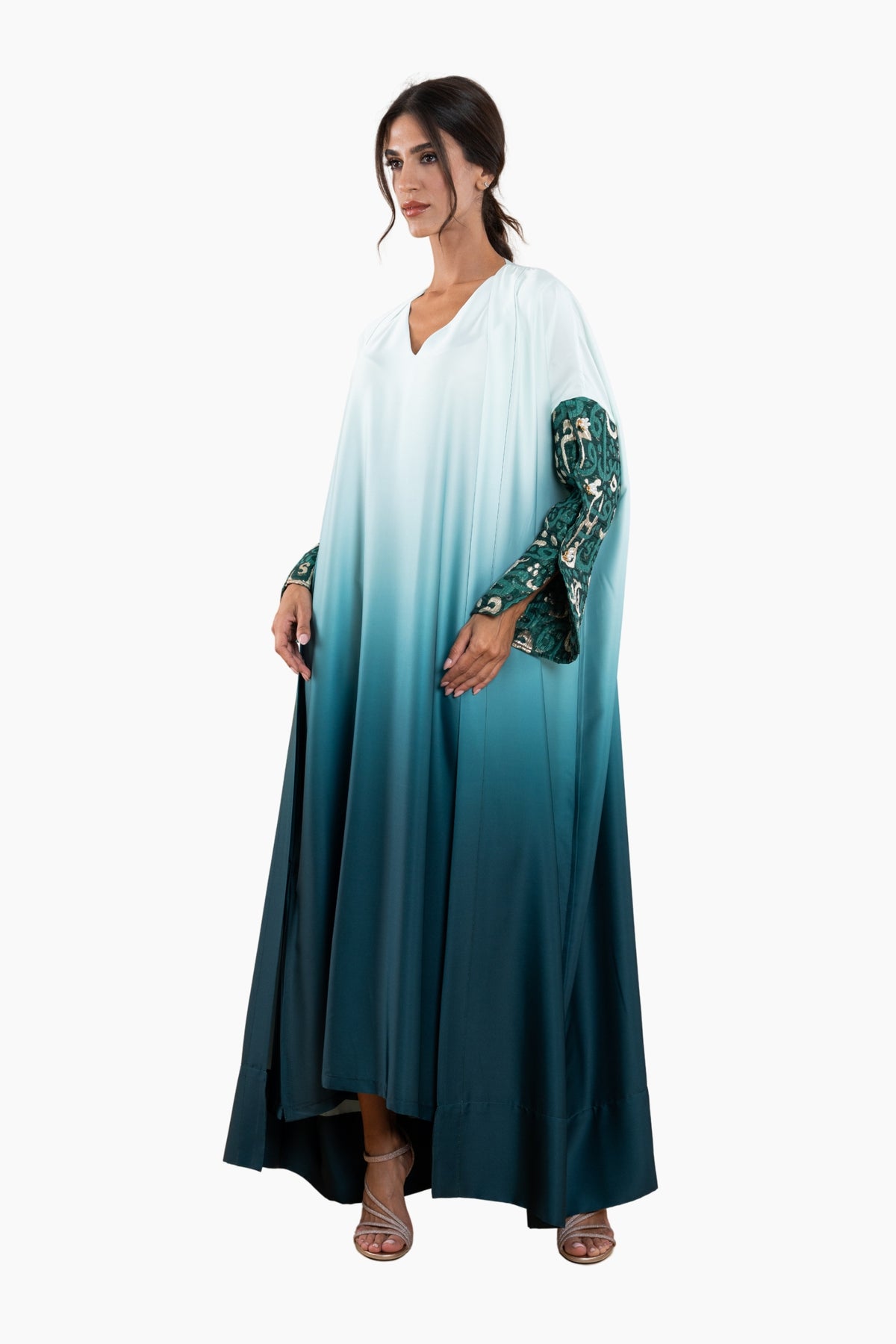Woman wearing a long, gradient dress with a white top and teal bottom on a white background