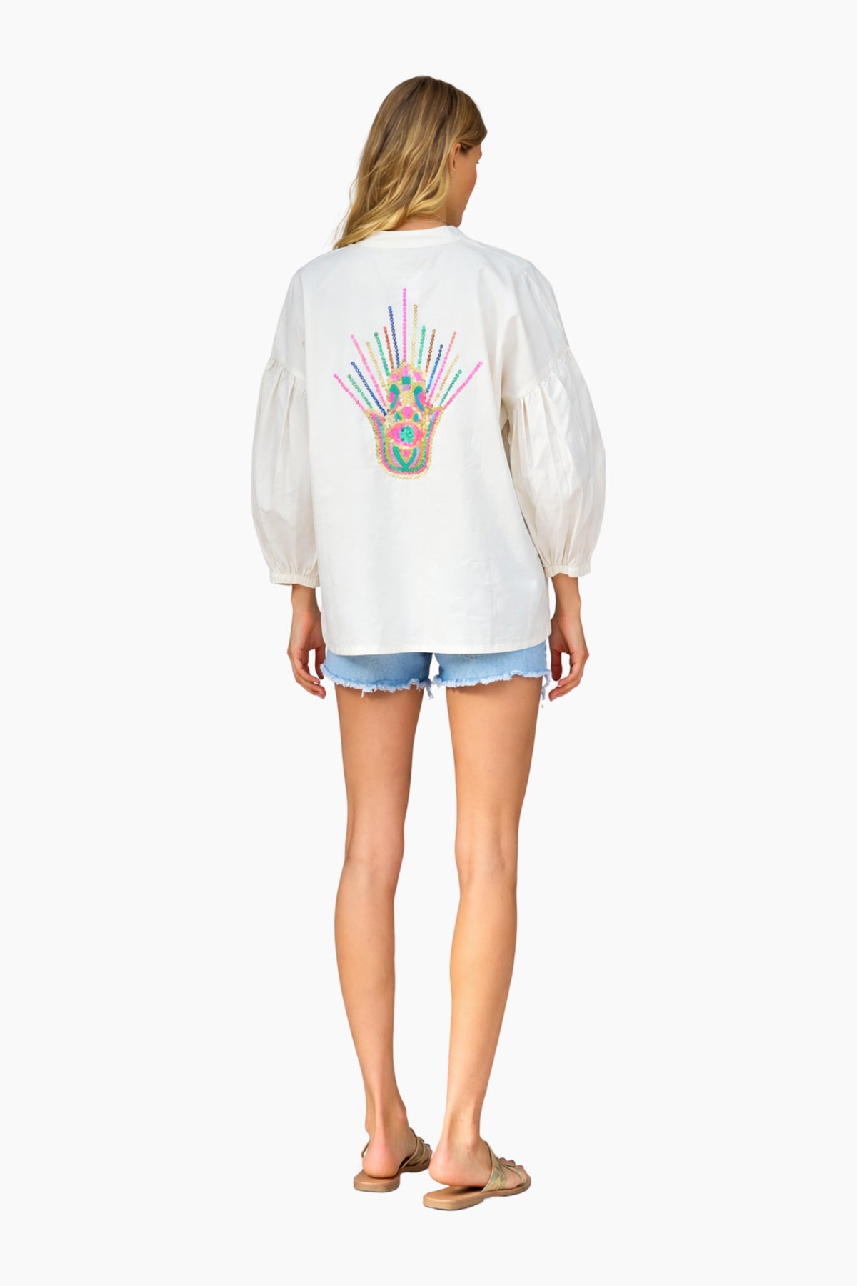 Woman wearing a white sweatshirt with a colorful design on the back, standing against a white background.