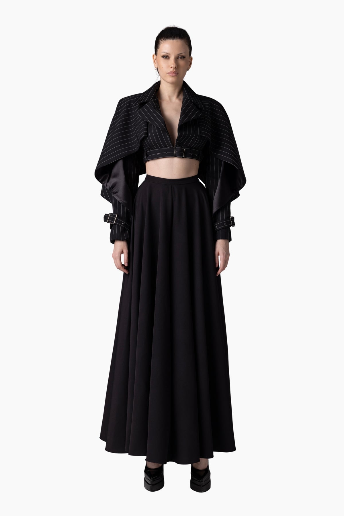 Woman wearing a black outfit with a long skirt and cropped jacket on a white background