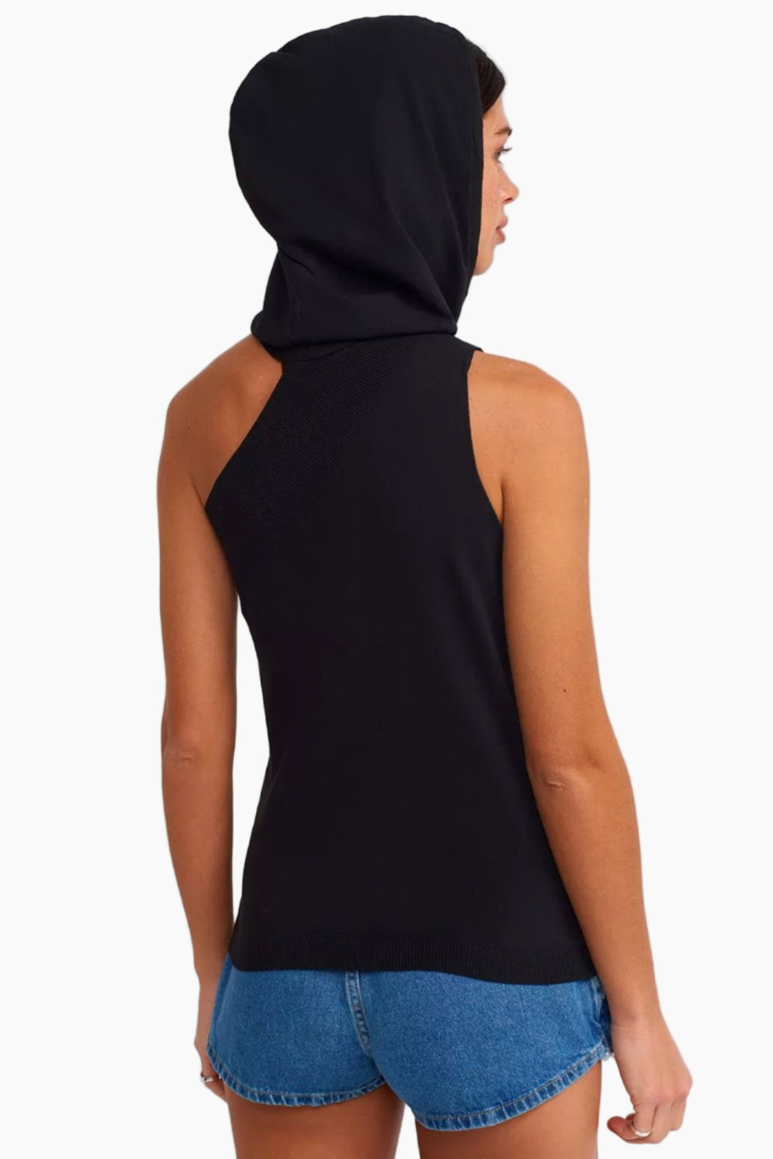 Person wearing a black sleeveless top with a hood and denim shorts on a white background