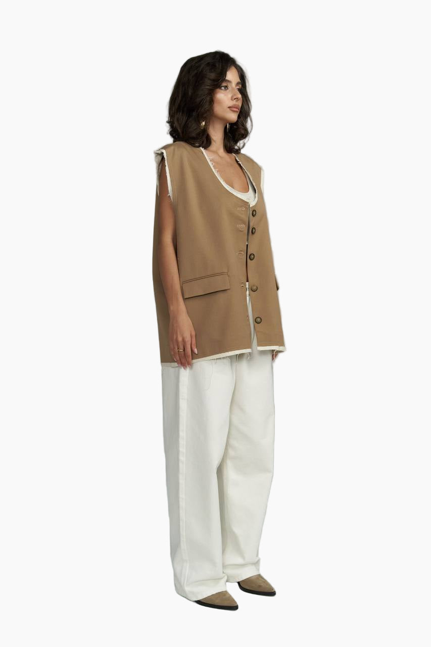 Woman wearing a beige vest over a white top and pants on a white background