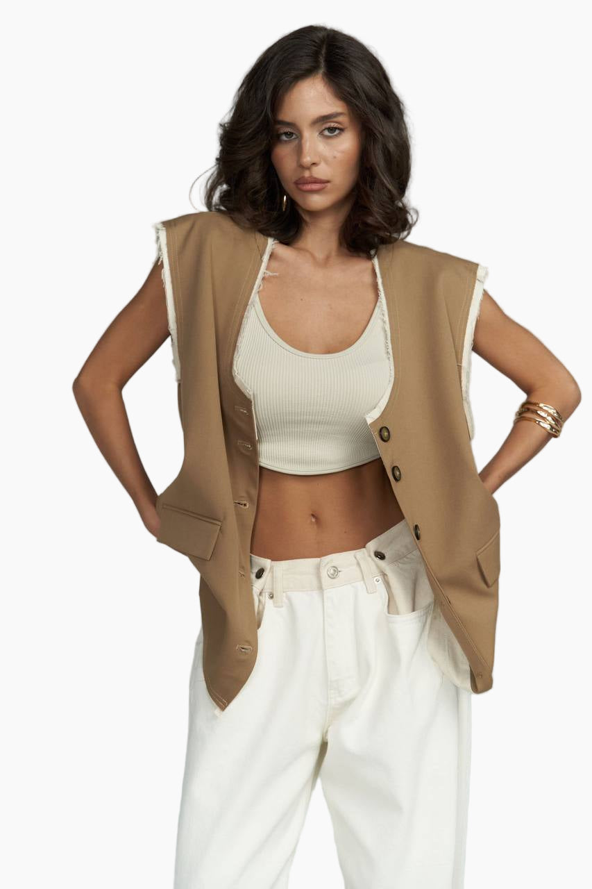 Woman wearing a beige vest over a white top and pants on a white background