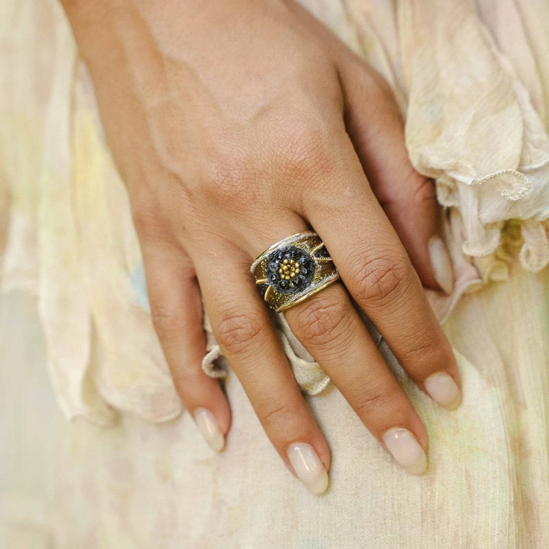Hand wearing a gold ring with a dark stone