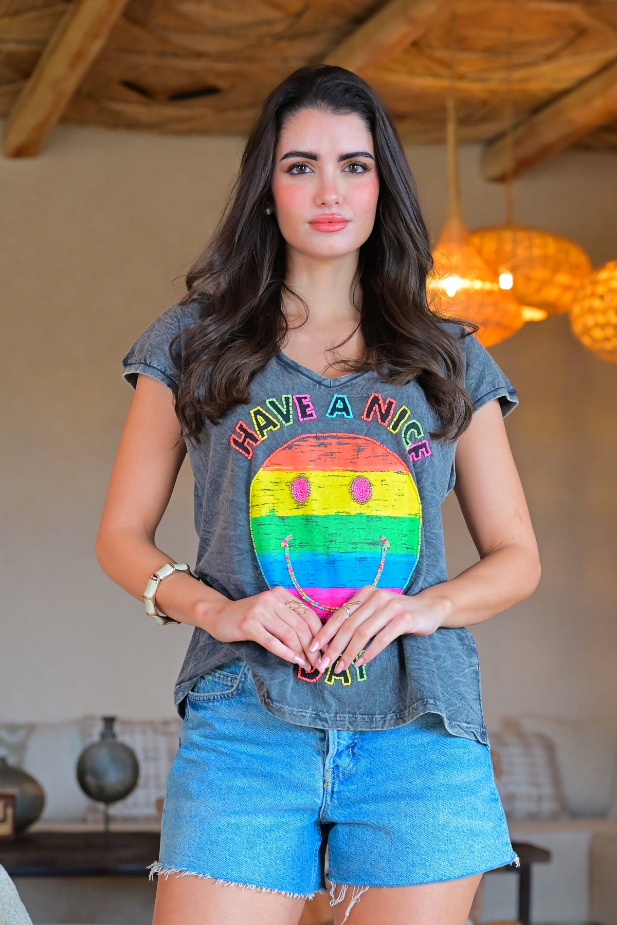 Woman wearing a t-shirt with a rainbow face design and text indoors.